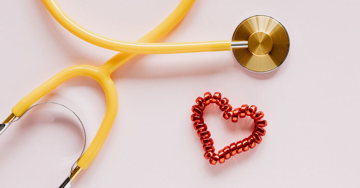 A yellow stethoscope and red heart decoration symbolize love and healthcare on soft pink.